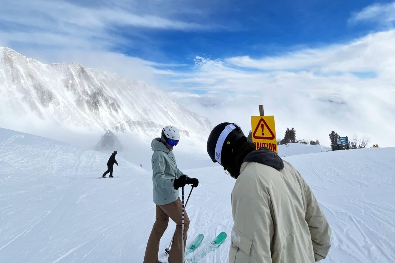 One skier, one snowboarder, standing at the top of a bowl in Big Sky, MT.